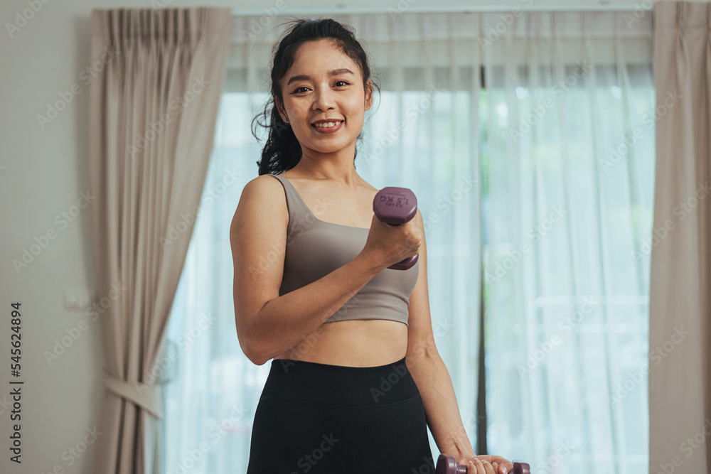 Asian woman exercise at home. Healthy female in sportswear workout training with dumbbell in living room, Health care and wellness concept.