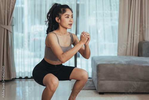 Asian woman exercise at home. Healthy female in sportswear doing squat workout in living room, Health care and wellness concept.
