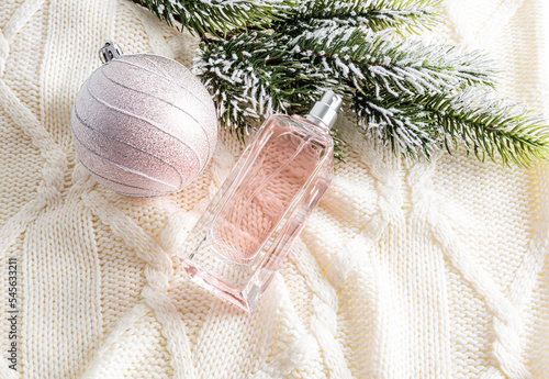winter New Year's advertising composition of women's perfumes on a knitted beige background with a beautiful ball and a branch of spruce.