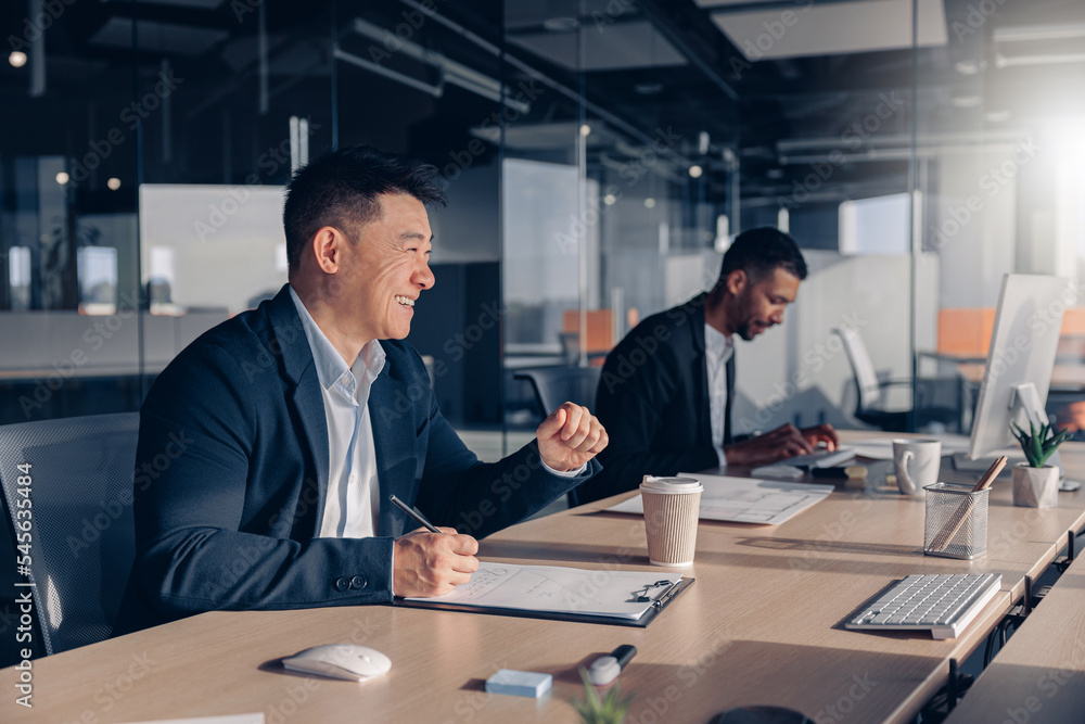 Smiling asian businessman drinking coffee while working with documents in modern office Smiling asian businessman drinking coffee while working with documents in modern office