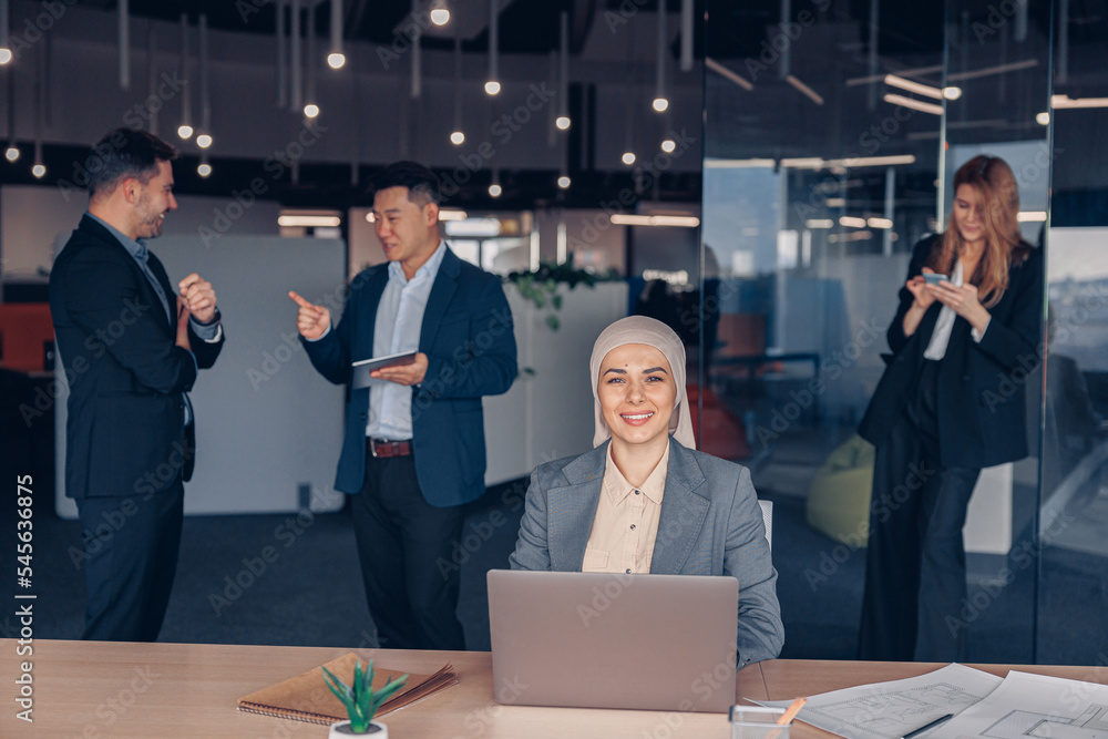 Smiling muslim businesswoman in hijab working on computer while sitting in modern office Smiling muslim businesswoman in hijab working on computer while sitting in modern office