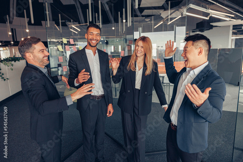 Group of smiling multietnic colleagues talking together during break time while standing in office