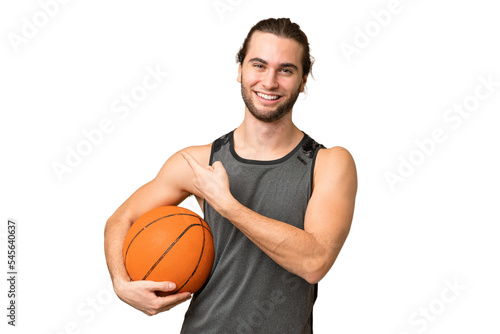 Young handsome man isolated on green chroma background playing basketball and pointing to the lateral © luismolinero