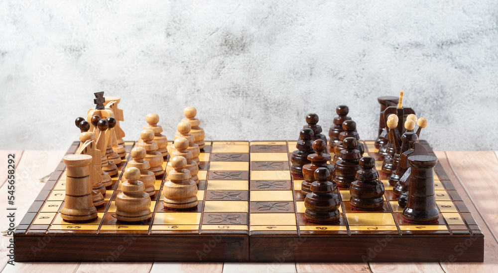 Hand-carved chess pieces on a handcrafted wooden chessboard. Business strategy, tactics concept Hand-carved chess pieces on a handcrafted wooden chessboard. Business strategy, tactics concept