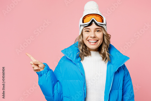 Snowboarder fun woman wear blue suit goggles mask hat ski padded jacket point index finger aside on area isolated on plain pastel pink background Winter extreme sport hobby weekend trip relax concept