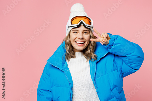 Snowboarder woman wear blue suit goggles mask hat ski padded jacket show cover eye with victory gesture isolated on plain pastel pink background. Winter extreme sport hobby weekend trip relax concept.
