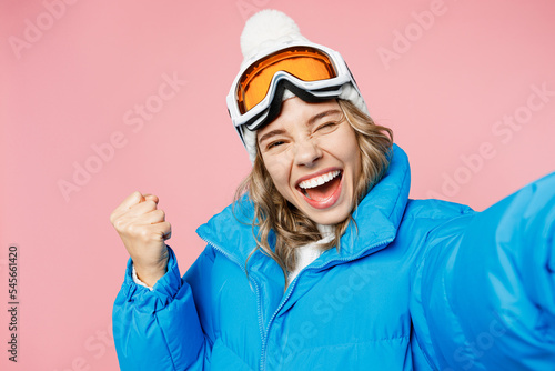 Close up winner snowboarder woman in blue suit goggles mask hat ski jacket do selfie shot pov mobile cell phone isolated on plain pastel pink background Winter extreme sport hobby trip relax concept