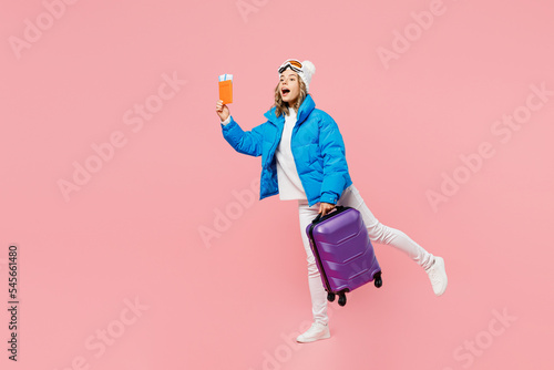 Snowboarder woman in blue suit goggles mask hat ski jacket hold passport ticket bag catch taxi isolated on pink background Tourist travel abroad in free time rest Air flight winter trip sport concept.