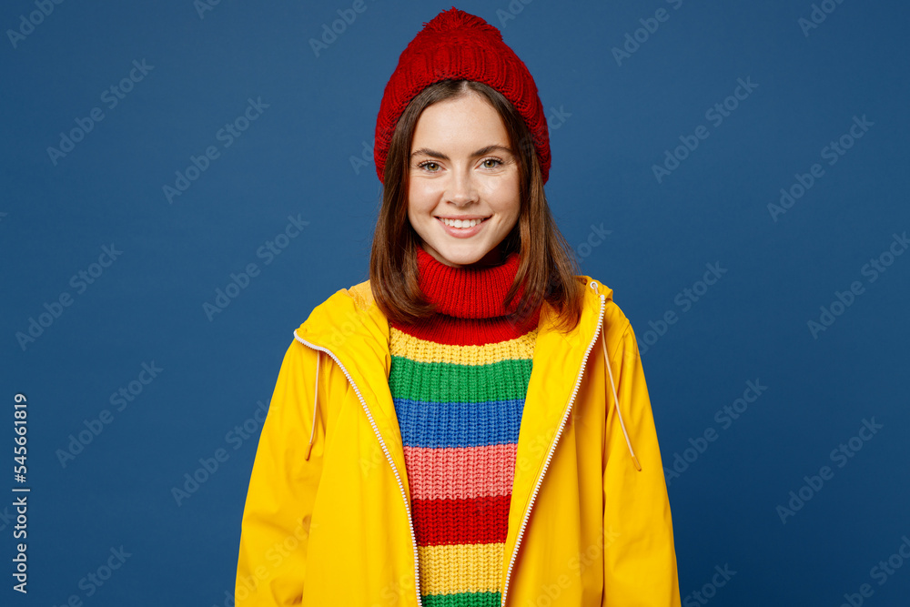 Young smiling happy cheerful fun woman wears sweater yellow waterproof raincoat outerwear red hat look camera isolated on plain dark royal navy blue background Outdoor wet fall weather season concept Young smiling happy cheerful fun woman wears sweater yellow waterproof raincoat outerwear red hat look camera isolated on plain dark royal navy blue background Outdoor wet fall weather season concept