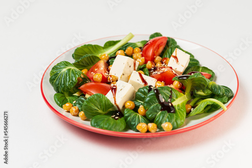 Fresh pak choi salad with tomatoes,chickpeas and feta cheese, poured with sauce and sesame seeds in a plate  isolated  on white