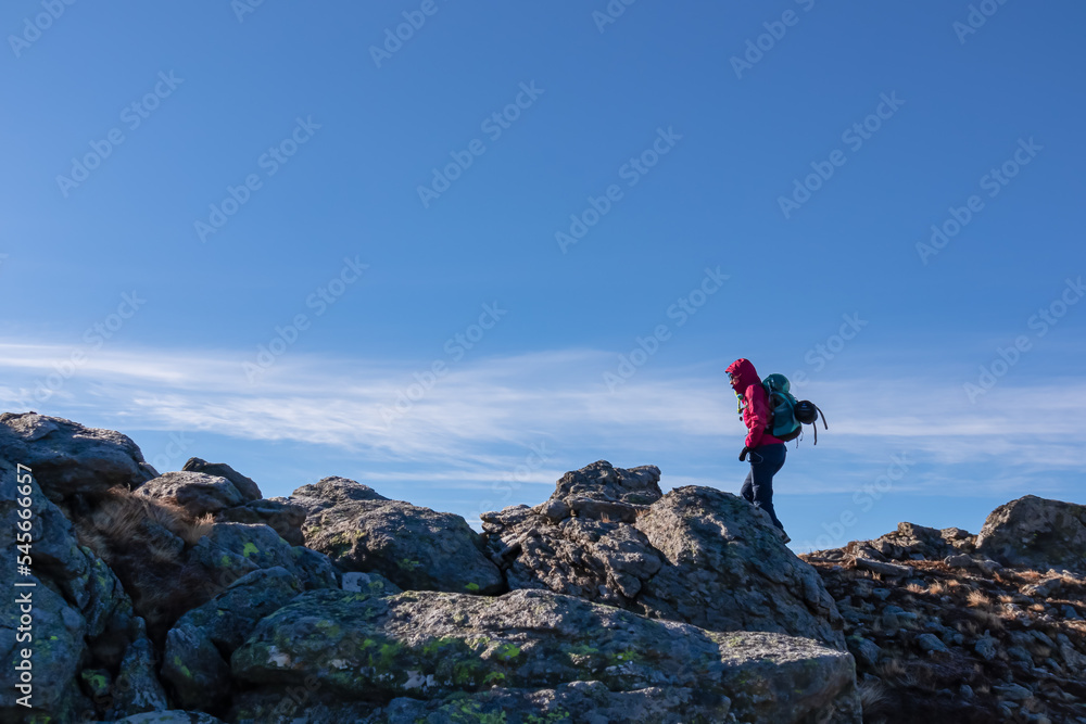 Woman with backpack and jacket hiking on rock formations from Ladinger Spitz to Gertrusk, Saualpe, Lavanttal Alps, Carinthia, Austria, Europe. Sunny cold early spring day. Trekking in Austrian Alps