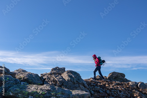 Woman with backpack and jacket hiking on rock formations from Ladinger Spitz to Gertrusk, Saualpe, Lavanttal Alps, Carinthia, Austria, Europe. Sunny cold early spring day. Trekking in Austrian Alps