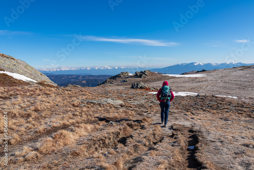 Woman hiking on frozen alpine meadow from Ladinger Spitz to Gertrusk, Saualpe, Lavanttal Alps, Carinthia, Austria, Europe. Morning frost on cold early spring day. Trekking in the Austrian Alps