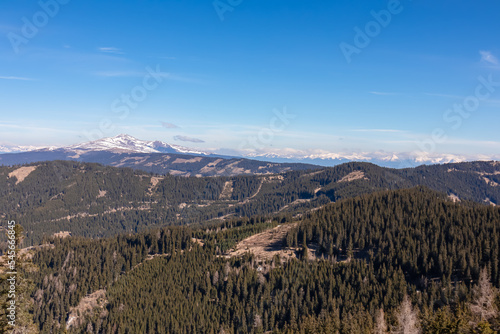 Panoramic view of forest and snow capped mountain peak Zirbitzkogel seen from Ladinger Spitz, Saualpe, Carinthia, Austria, Europe. Alpine hiking trail in Central Alps in early spring on sunny day