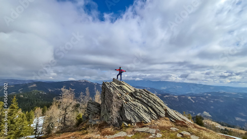 Woman with backpack standing on massive rock formation at Steinerne Hochzeit, Saualpe, Lavanttal Alps, border Styria Carinthia, Austria, Europe. Panorama of alpine meadows and snowcapped mountains