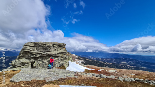 Woman with backpack resting next to massive rock formation at Steinerne Hochzeit, Saualpe, Lavanttal Alps, border Styria Carinthia, Austria, Europe. Panorama of alpine meadows and snowcapped mountains photo