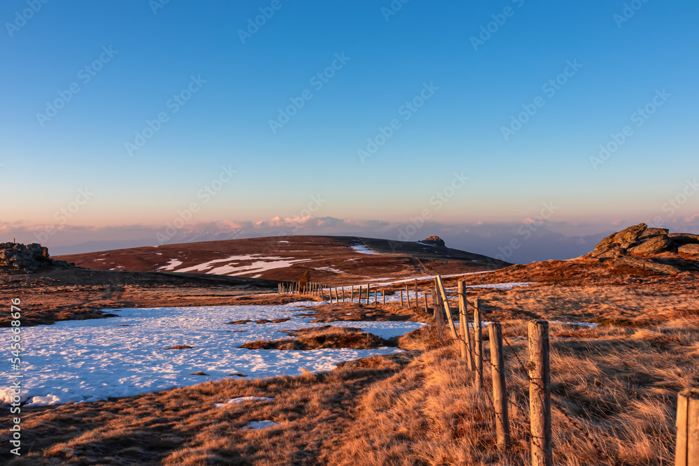 Fence on golden alpine pasture with scenic morning view after sunrise on summit cross of mountain peaks Grosser Sauofen, Saualpe, Lavanttal Alps, Carinthia, Austria, Europe. Hiking trail Wolfsberg