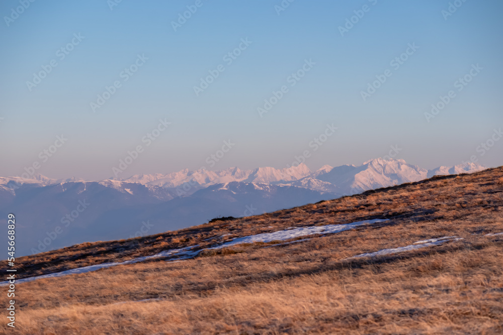 Panoramic view of the Schladminger Tauern mountain range at early morning after sunrise seen from Saualpe, Lavanttal Alps, Carinthia, Austria, Europe. Snowcapped mountain peaks and golden pasture