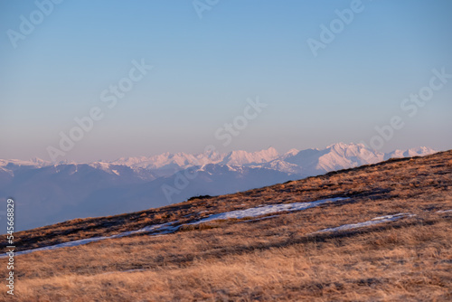 Panoramic view of the Schladminger Tauern mountain range at early morning after sunrise seen from Saualpe, Lavanttal Alps, Carinthia, Austria, Europe. Snowcapped mountain peaks and golden pasture