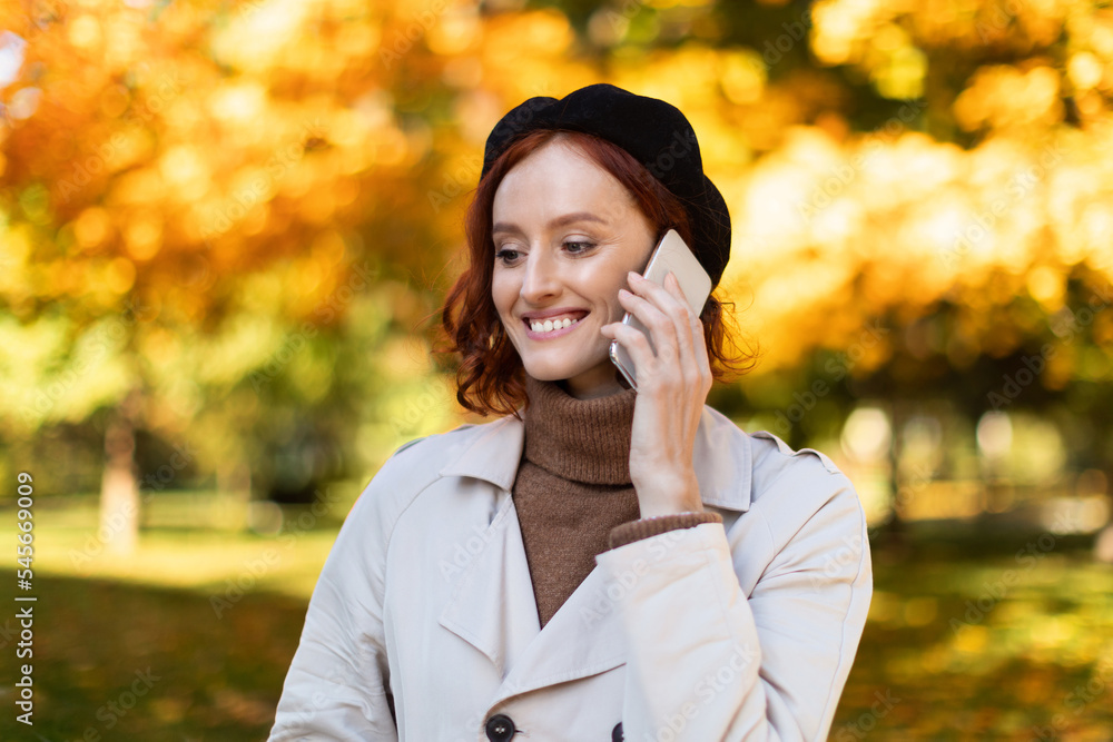 Cheerful pretty caucasian millennial female with red hair in raincoat and hat calling by phone, enjoy autumn Cheerful pretty caucasian millennial female with red hair in raincoat and hat calling by phone, enjoy autumn