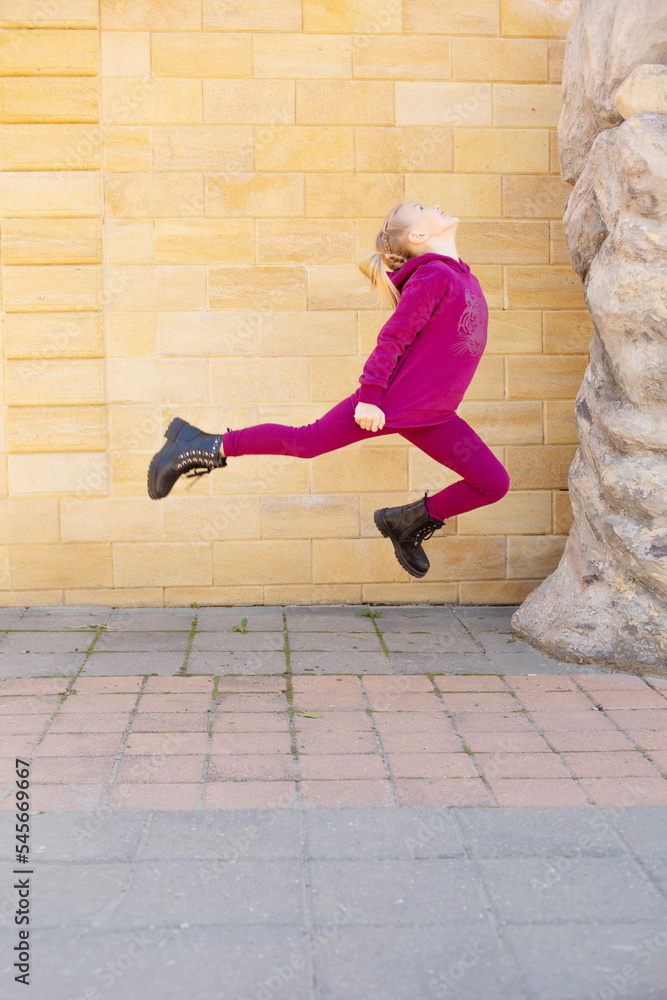 a blonde girl in a red suit performs acrobatic elements on the background of a brick wall a blonde girl in a red suit performs acrobatic elements on the background of a brick wall
