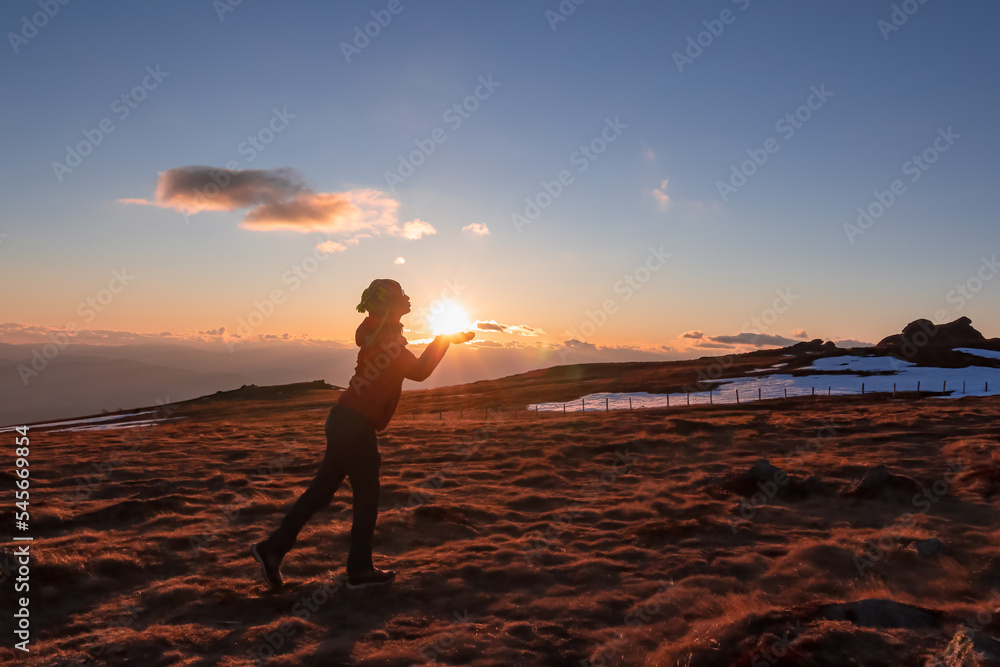 Silhouette of woman holding and kissing sun during sunset on mountain peak Ladinger Spitz, Saualpe, Lavanttal Alps, Carinthia, Austria, Europe. Warm atmosphere, inspiration, goal seeking concept