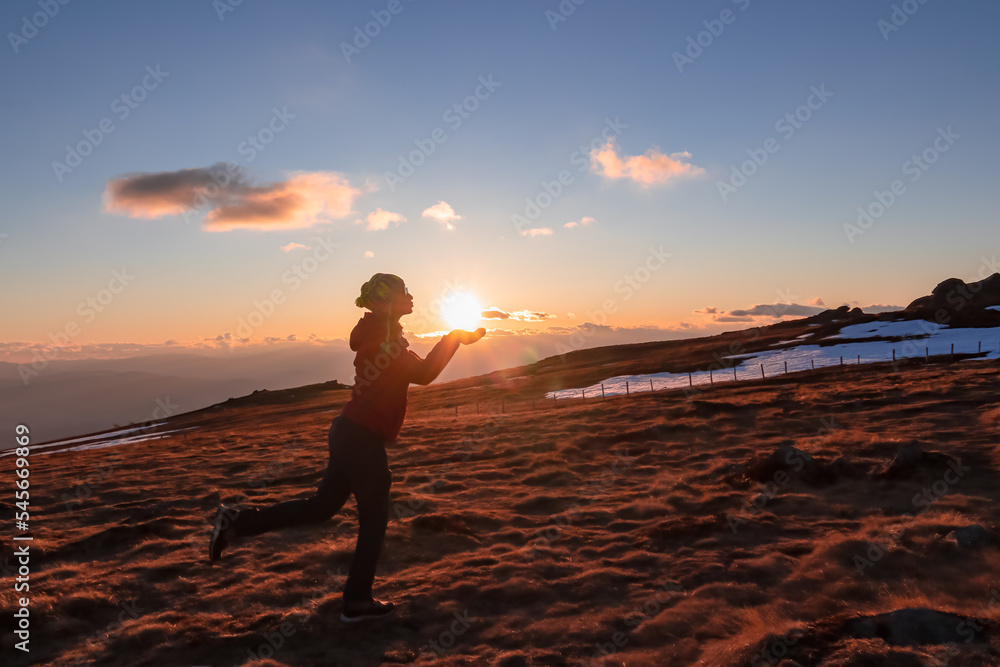 Silhouette of woman holding and kissing sun during sunset on mountain peak Ladinger Spitz, Saualpe, Lavanttal Alps, Carinthia, Austria, Europe. Warm atmosphere, inspiration, goal seeking concept