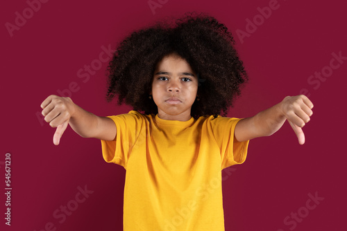 Disappointed african american kid showing thumb downs on colorful background