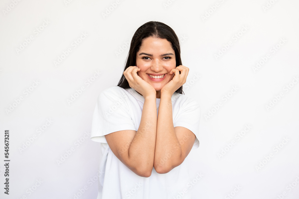 Portrait of cheerful young woman looking at camera and smiling over white background. Caucasian lady wearing white T-shirt touching face and laughing. Happiness concept Portrait of cheerful young woman looking at camera and smiling over white background. Caucasian lady wearing white T-shirt touching face and laughing. Happiness concept
