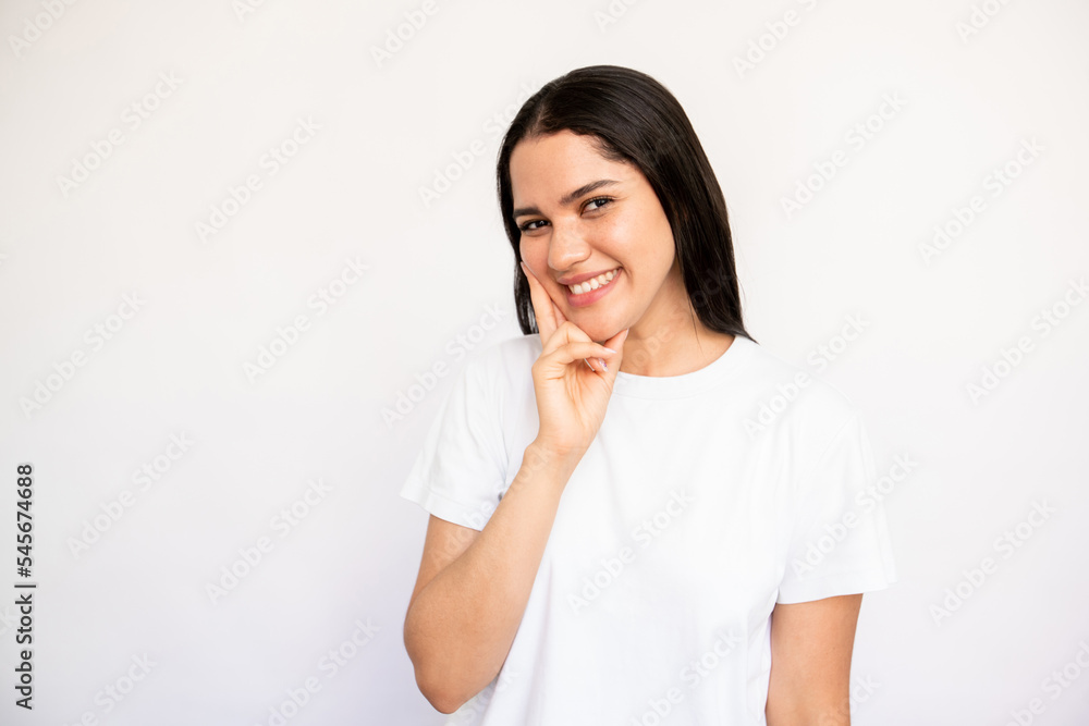 Portrait of happy young woman looking at camera with interest over white background. Caucasian lady wearing white T-shirt touching chin and smiling. Curiosity concept Portrait of happy young woman looking at camera with interest over white background. Caucasian lady wearing white T-shirt touching chin and smiling. Curiosity concept