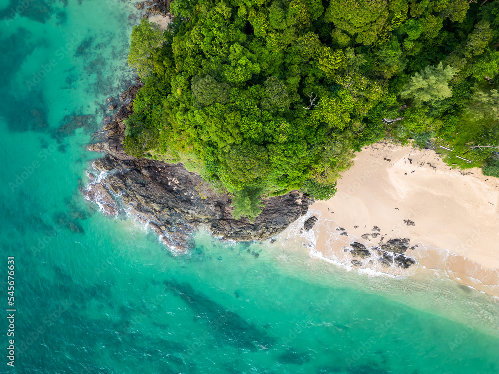 Aerial top down view of tropical beach with turquoise water, white sand and big rock. Trees and palms growing on the rock. Tropical theme.
