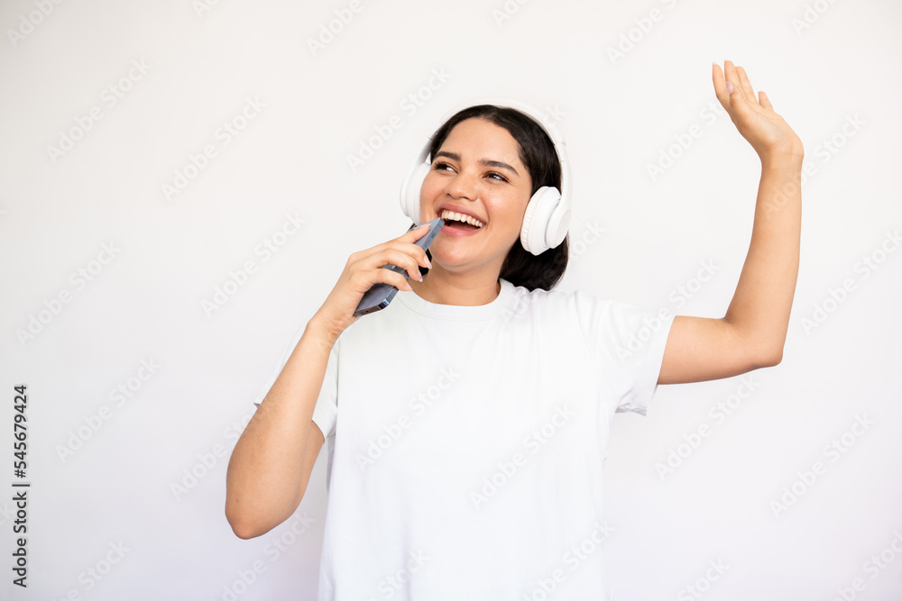 Portrait of happy woman in headphones singing in smartphone over white background. Young Caucasian lady wearing white T-shirt listening to mp3 player and dancing. Mobile technology and leisure concept Portrait of happy woman in headphones singing in smartphone over white background. Young Caucasian lady wearing white T-shirt listening to mp3 player and dancing. Mobile technology and leisure concept