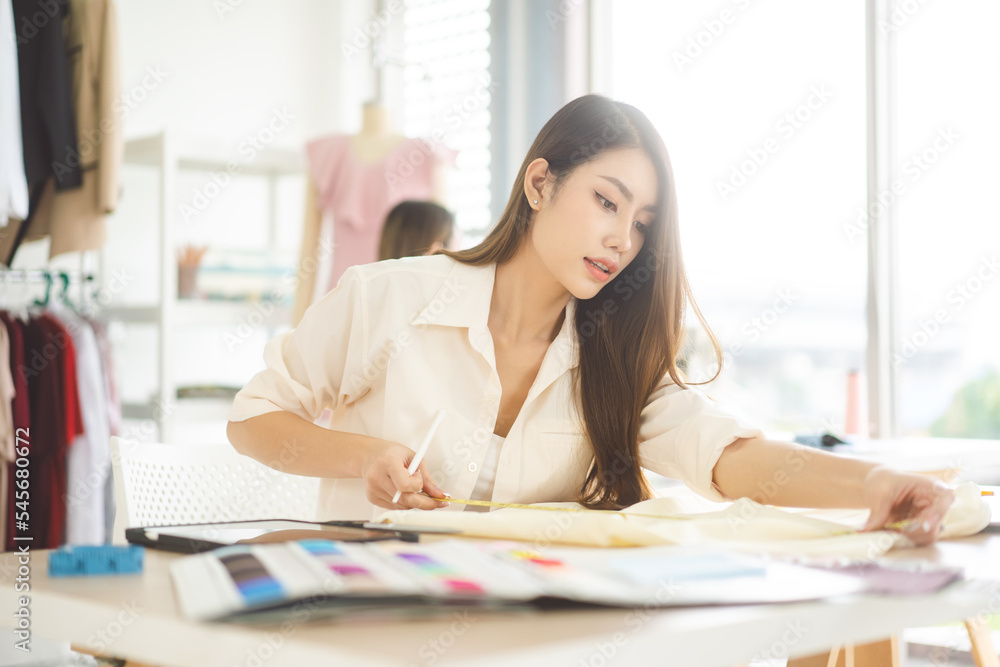 Fototapeta premium Young adult asian woman designer sit and making clothes tailor working in fashion design studio