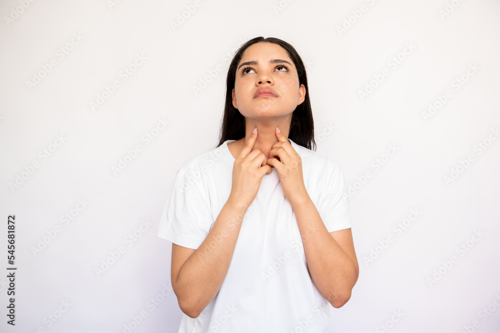 Portrait of serious young woman touching her throat over white background. Caucasian lady wearing white T-shirt suffering from pain in neck. Pulmonary diseases concept Portrait of serious young woman touching her throat over white background. Caucasian lady wearing white T-shirt suffering from pain in neck. Pulmonary diseases concept
