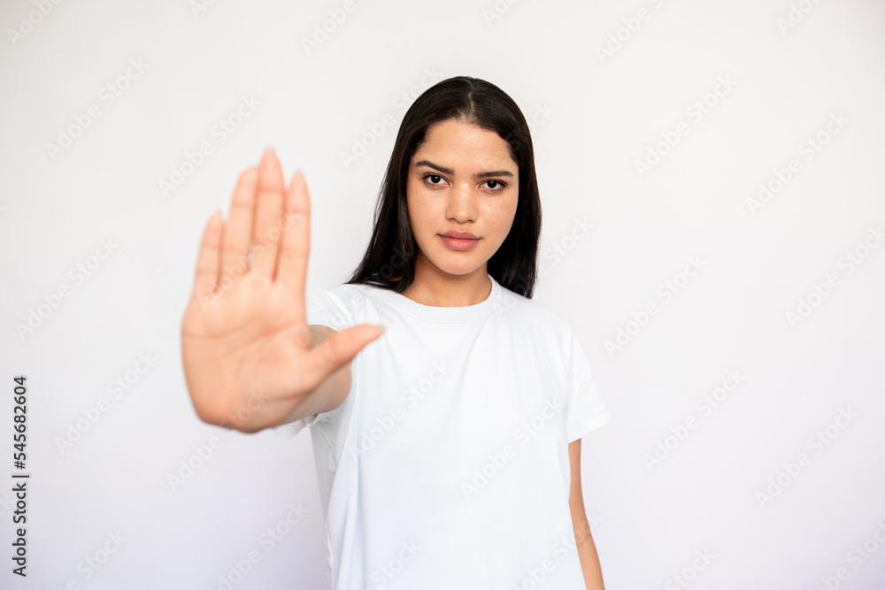 Portrait of confident young woman making refusal gesture over white background. Caucasian lady wearing white T-shirt showing stop gesture. Forbiddance and restriction concept Portrait of confident young woman making refusal gesture over white background. Caucasian lady wearing white T-shirt showing stop gesture. Forbiddance and restriction concept