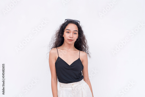 A slim and confident Filipino woman with long curly hair in her early 20s. Wearing a black spaghetti strap blouse and white pants. Isolated on a white background.