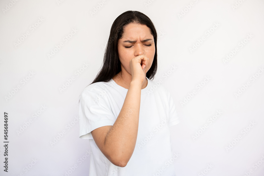 Portrait of sick young woman coughing and covering mouth with hand over white background. Caucasian lady wearing white T-shirt suffering from cold or flu. Pulmonary diseases concept Portrait of sick young woman coughing and covering mouth with hand over white background. Caucasian lady wearing white T-shirt suffering from cold or flu. Pulmonary diseases concept