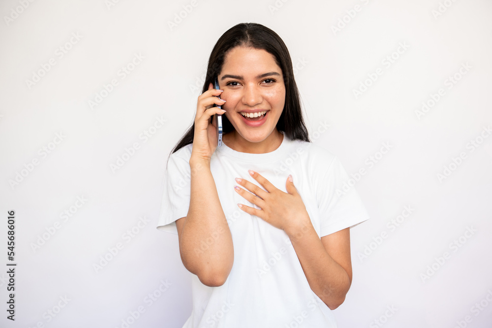 Portrait of cheerful young woman talking on mobile phone over white background. Caucasian lady wearing white T-shirt holding smartphone, looking at camera and smiling. Mobile communication concept Portrait of cheerful young woman talking on mobile phone over white background. Caucasian lady wearing white T-shirt holding smartphone, looking at camera and smiling. Mobile communication concept