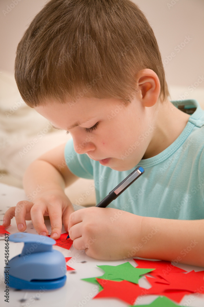 A cute baby writes a Happy New Year on a star cut out of paper. Preparation of decor and gifts for Christmas and New Year holidays. Close-up. A cute baby writes a Happy New Year on a star cut out of paper. Preparation of decor and gifts for Christmas and New Year holidays. Close-up.