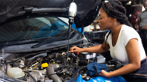 African female auto mechanic worker checking oil level in car engine at Car Service station. Car maintenance and auto service garage concept. © NVB Stocker