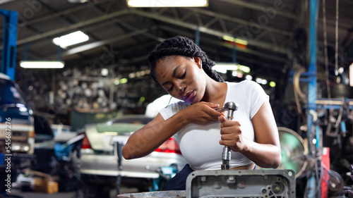 African young female car mechanic checking and fixing car engine at service car garage. Black woman mechanic working in car service and maintenance workshop.