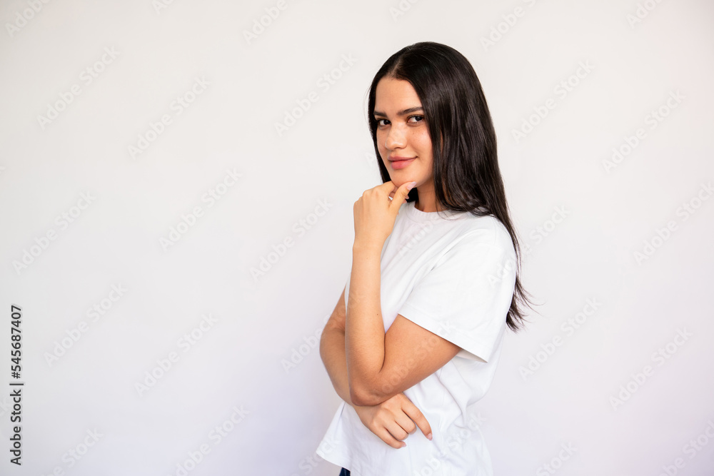 Portrait of young woman looking at camera with flirty expression. Caucasian lady wearing white T-shirt posing with hand on chin over white background. Interest concept Portrait of young woman looking at camera with flirty expression. Caucasian lady wearing white T-shirt posing with hand on chin over white background. Interest concept