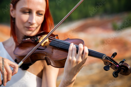 a young red-haired violinist plays the violin with her eyes closed against the background of the Martian landscape and the forest during the day