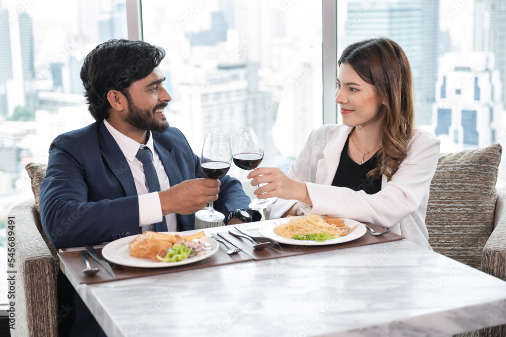 Asia businesswoman and Arab businessman cheers with husband at restaurant and city out of window background	