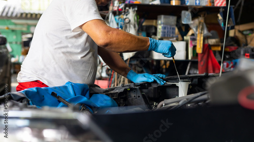 Senior asian male auto mechanic worker checking oil level in car engine at Car Service station. Car maintenance and auto service garage concept. © NVB Stocker