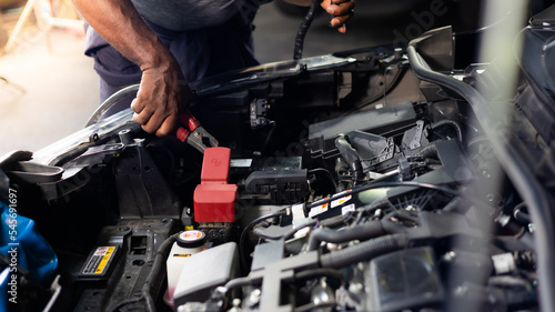 African american mechanic man uses multimeter voltmeter to check voltage level in car battery at car service and maintenance garage.
