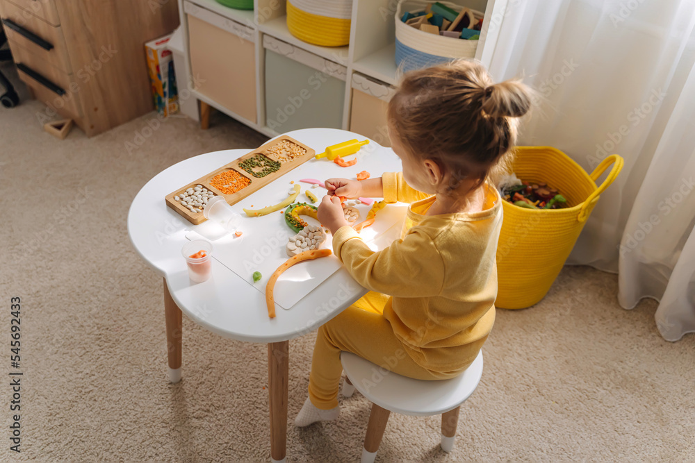A little girl playing with rainbow from play dough for modeling with decorate from dried beans