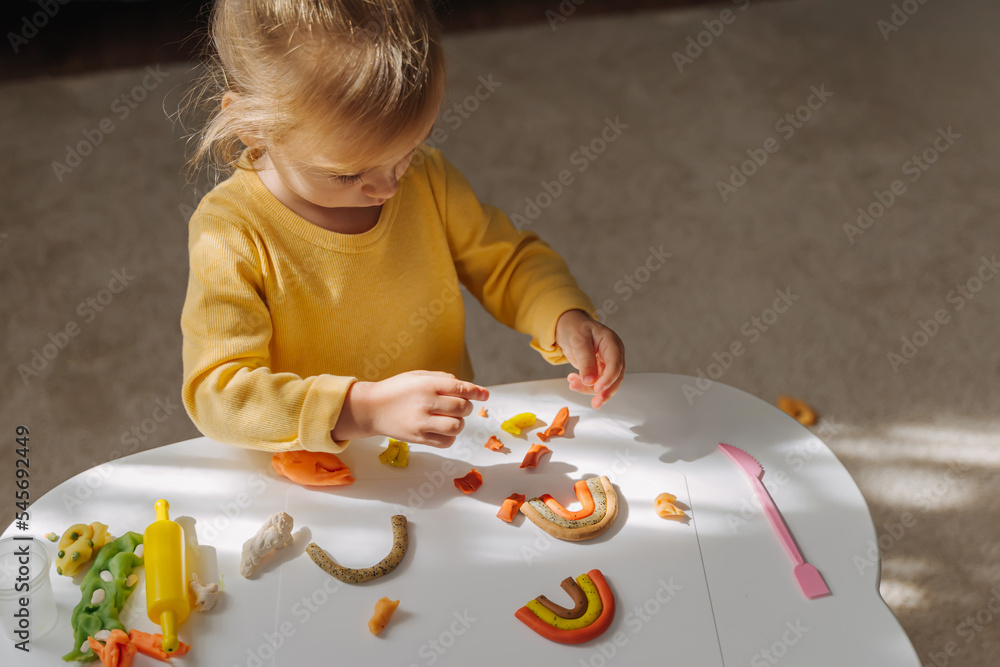 A little girl playing with rainbow from play dough for modeling. Art Activity for Kids. Fine