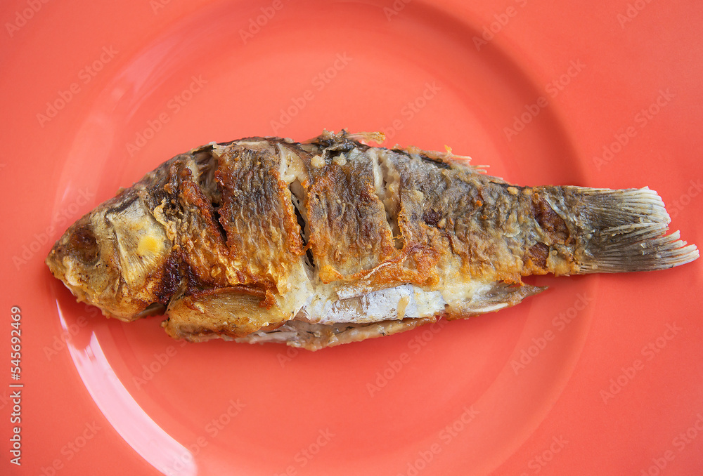 A whole fried carp with a fried crust, served on a bright red plate. View from above. A whole fried carp with a fried crust, served on a bright red plate. View from above.