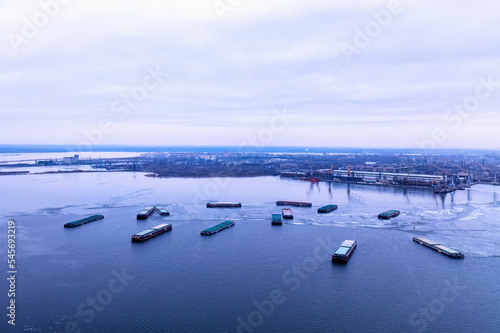 A cargo ships standing on a frozen river. Freight transportation concept, import export and business logistics, aerial view in winter. Nikolaev, Ukraine